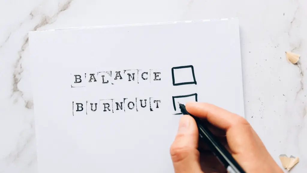 Een vel papier met daarop de woorden Balance en Burn-out gedrukt met naast elk een leeg vakje waarboven een hand met een pen zweeft.
