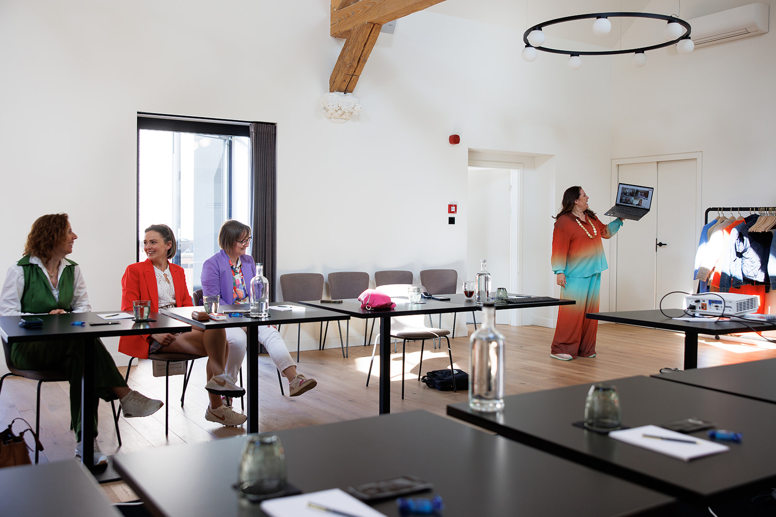Freelance Office collega's die tijdelijke hulp bieden zijn in vergadering in een grote zaal, zaakvoerster Saartje houdt een laptop omhoog.