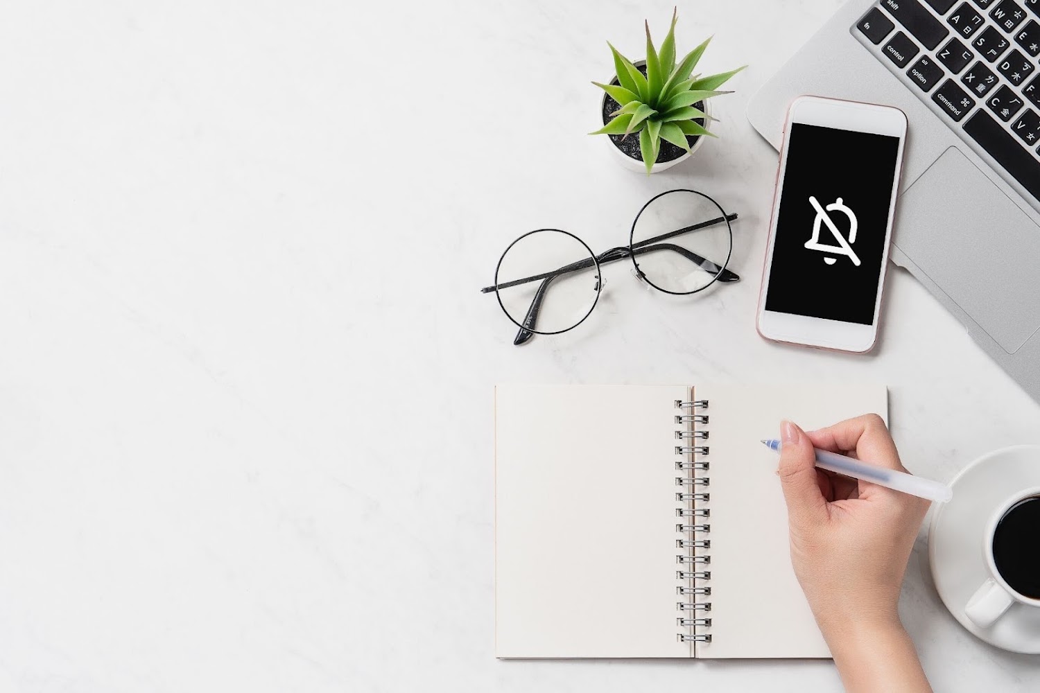 Een bureau met laptop, bril, plant en notitieboekje. Een telefoonscherm laat een notifications off icoon zien voor een betere work-life balance