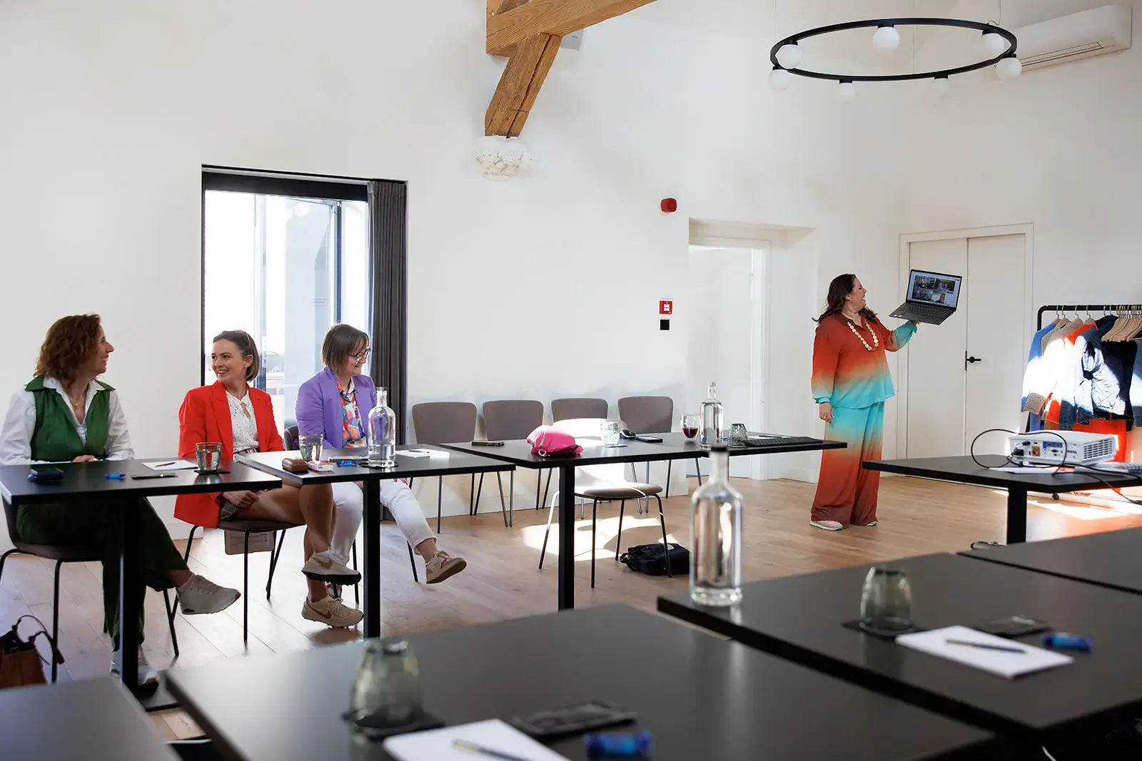 Een groepje dames zit links en rechts staat een onderneemster met een laptop in haar hand