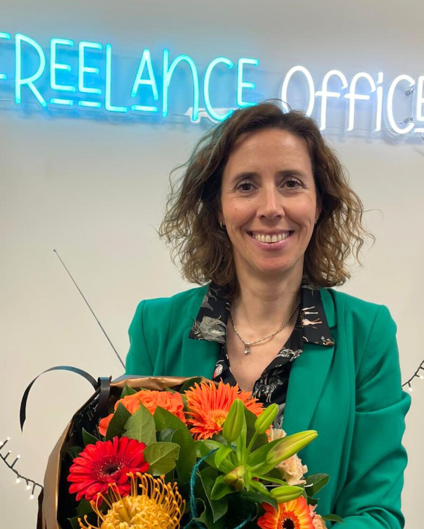een dame met krullend haar houdt een bloemenboeket vast met achter haar een neon-licht met het Freelance Office logo